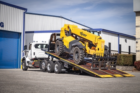 This image shows a century R30 industrial carrier with the bed deployed loading a telehandler.