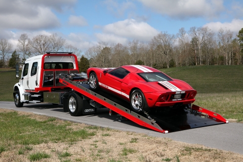 white and red century 12 series lcg with right approach option on a freightliner m2 chassis loaded with a red ford gt
