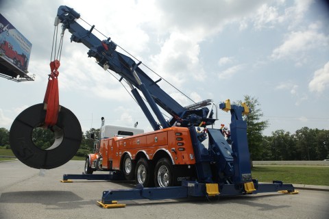 orange white and blue century 1150 rotator lifting a steel coil off of the side