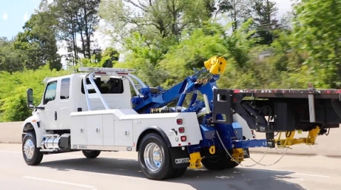 Image shows a Century®️ 3212 medium-duty wrecker towing a stake bed truck down the interstate.