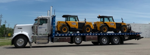 Image shows tow front end loaders being carried on the back of a Century 40-series industrial carrier equipped with a tag axle.