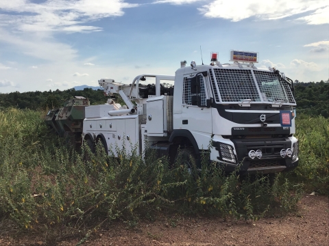 Image of a Century 1135 towing an armored military vehicle through rough overgrown terrain and brush.