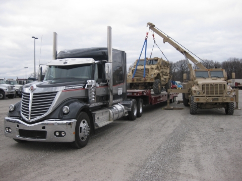 A Century 1135 lifting and loading a military APC on the back of a truck bed for transport