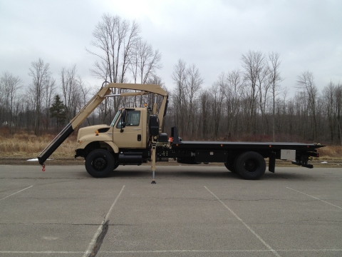 Side view of a Century Military carrier with the recovery arm reaching of the front of the hood of the truck cab