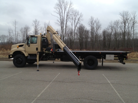 Side image of a Century military carrier with outriggers extended and recovery arm reaching over the the side