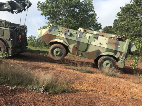 A military Century 1140 rotator towing an armored military vehicle up a steep hill