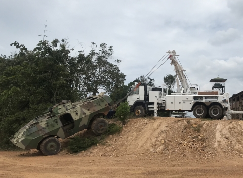 A Century 1135 rotator winching a damaged armored military vehicle up a steep inclined hill while conducting a recovery.