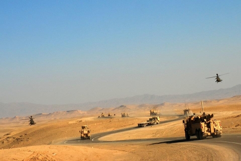 Image shows a convoy of military vehicles, a Century 1135 rotator, and helicopters in a conflict zone