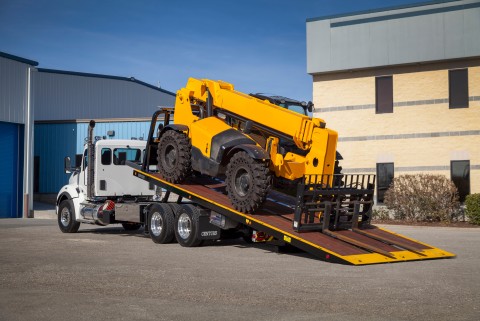 This image shows the Century R30 industrial carrier carrying a telehandler on a wooden deck