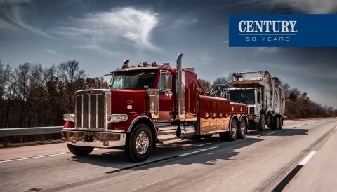 Red Century 5130 on a Peterbilt 589 chassis towing a trash truck on the highway