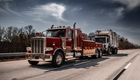 Red Century 5130 on a Peterbilt 589 chassis towing a trash truck down the highway